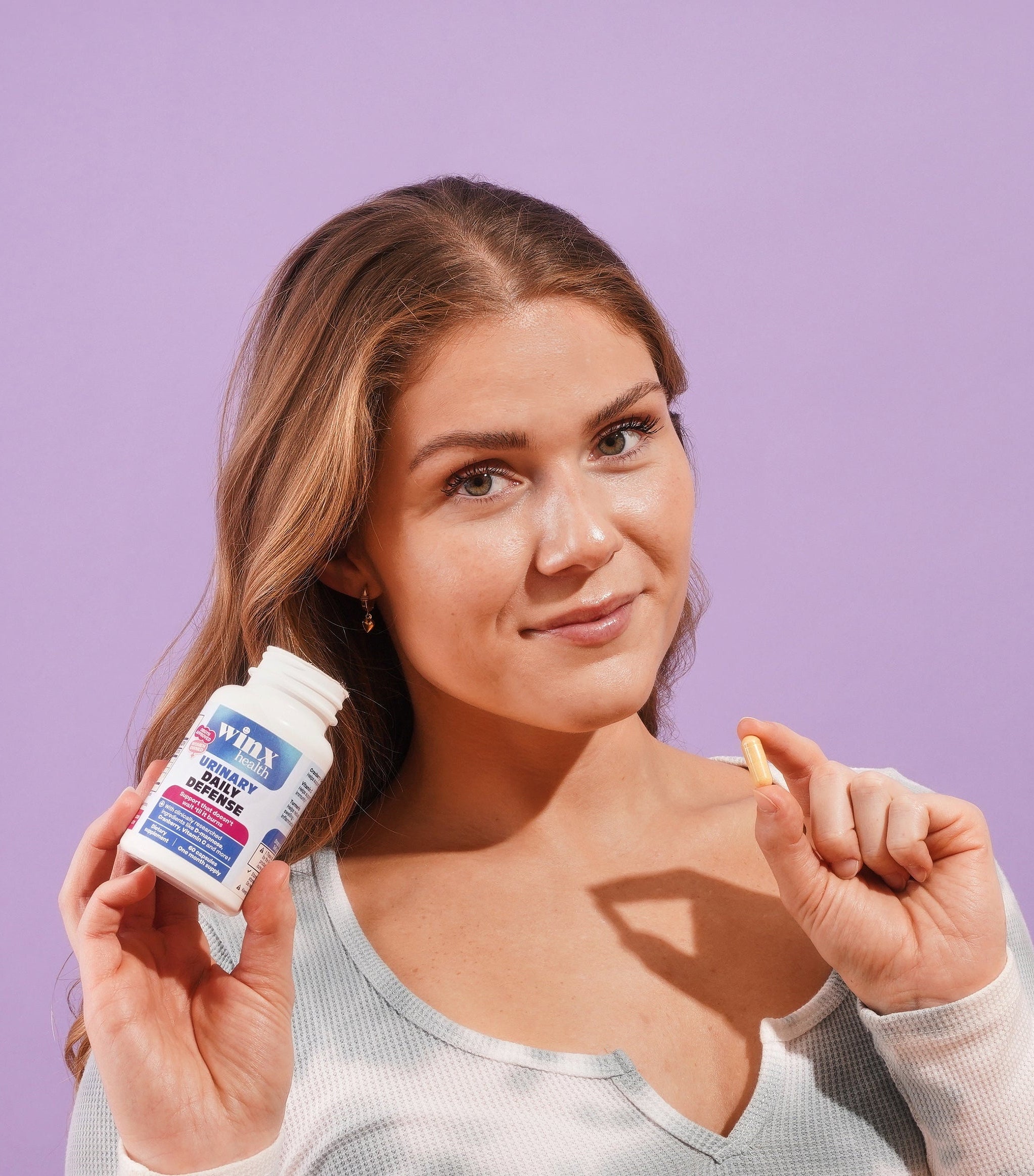 Woman holding a bottle of supplements against a purple background